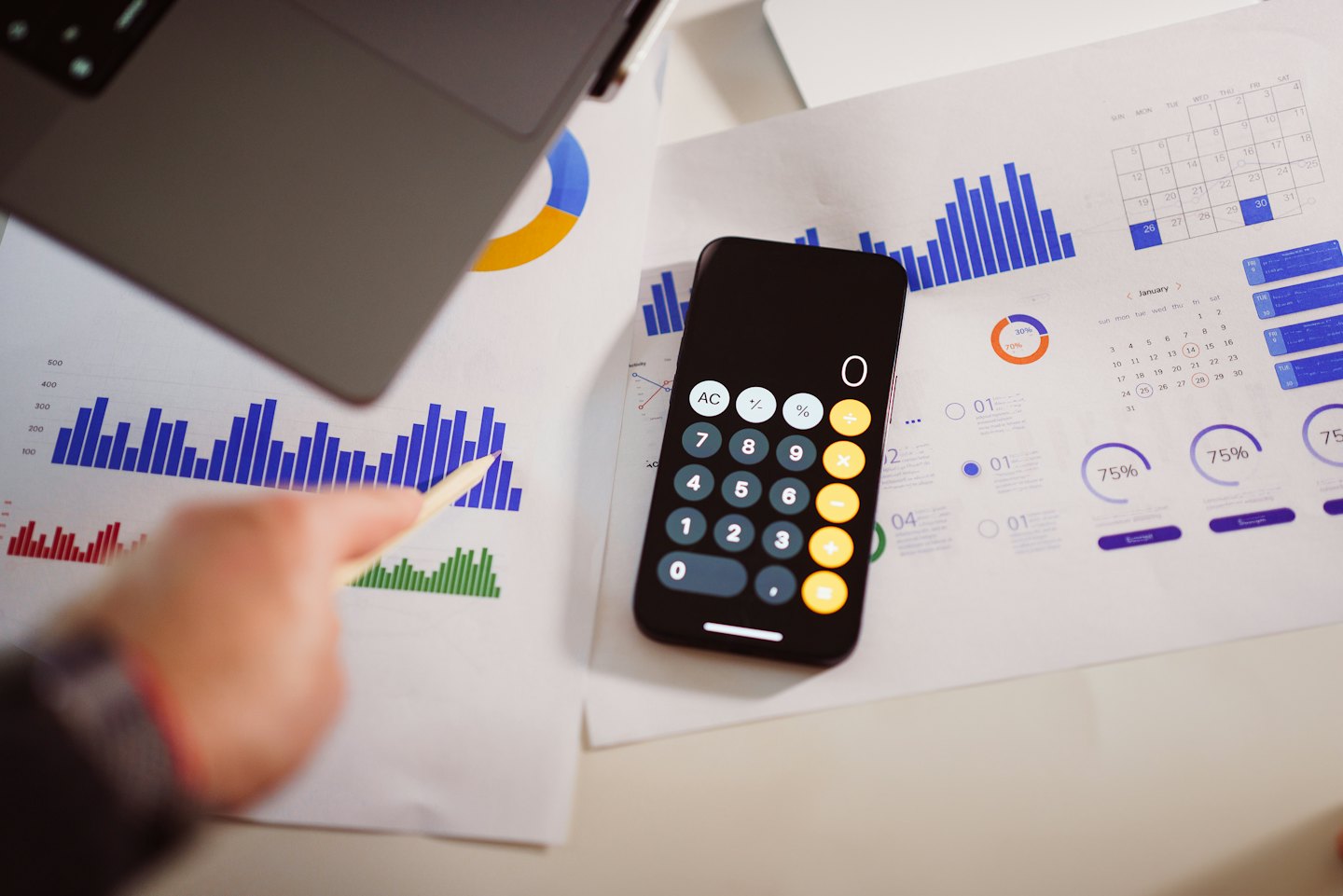 Hand pointing to bar chart with laptop and smartphone.